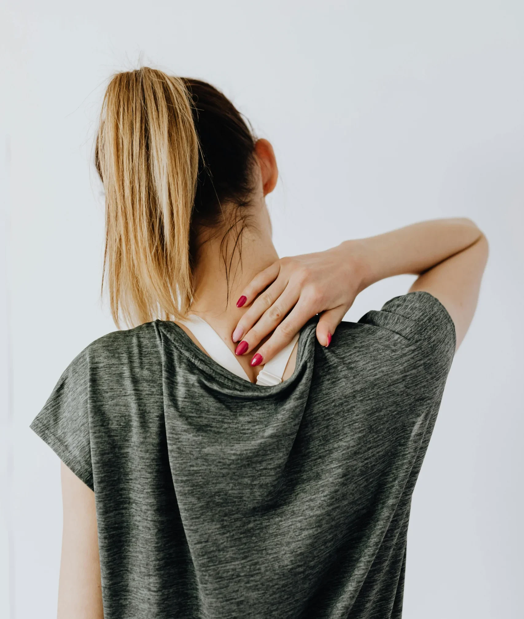 Woman holding her neck in pain – A woman with her back turned, holding her neck in discomfort.